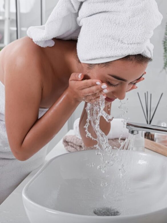 Beautiful young woman washing her face with water in bathroom