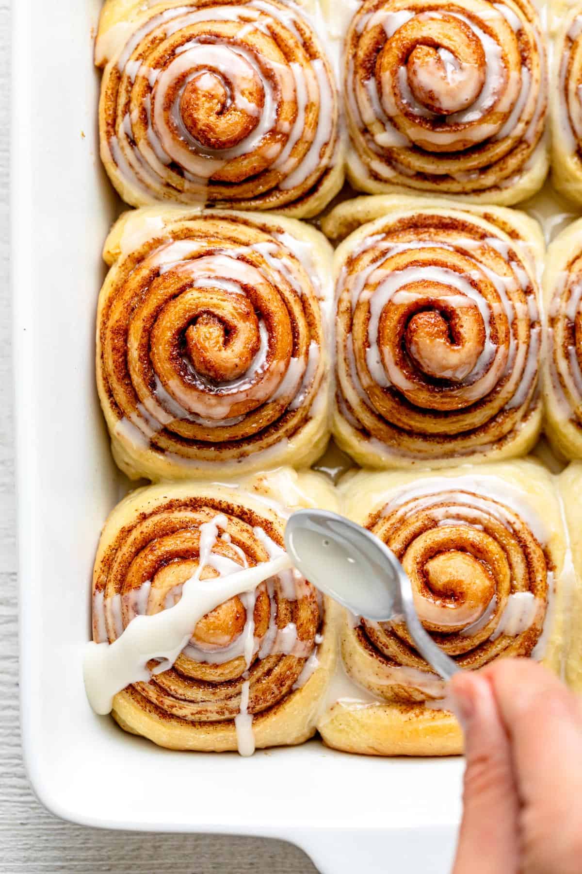 Vegan cinnamon rolls in a pan getting icing poured all over