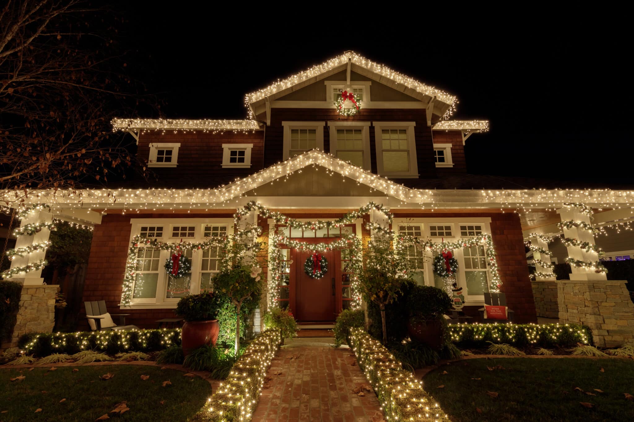 Christmas decorations with lights and reefs outside of a home with a pathway to the front door.
