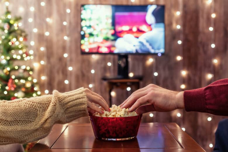 couple reaching for popcorn while watching Christmas movies