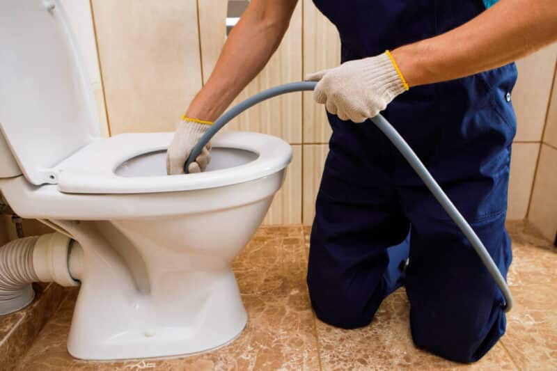 plumber unclogging blocked toilet with hydro jetting at home bathroom. 