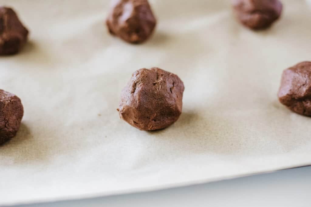 Cookie sheet lined with parchment paper and filled with chocolate cookie dough balls. 