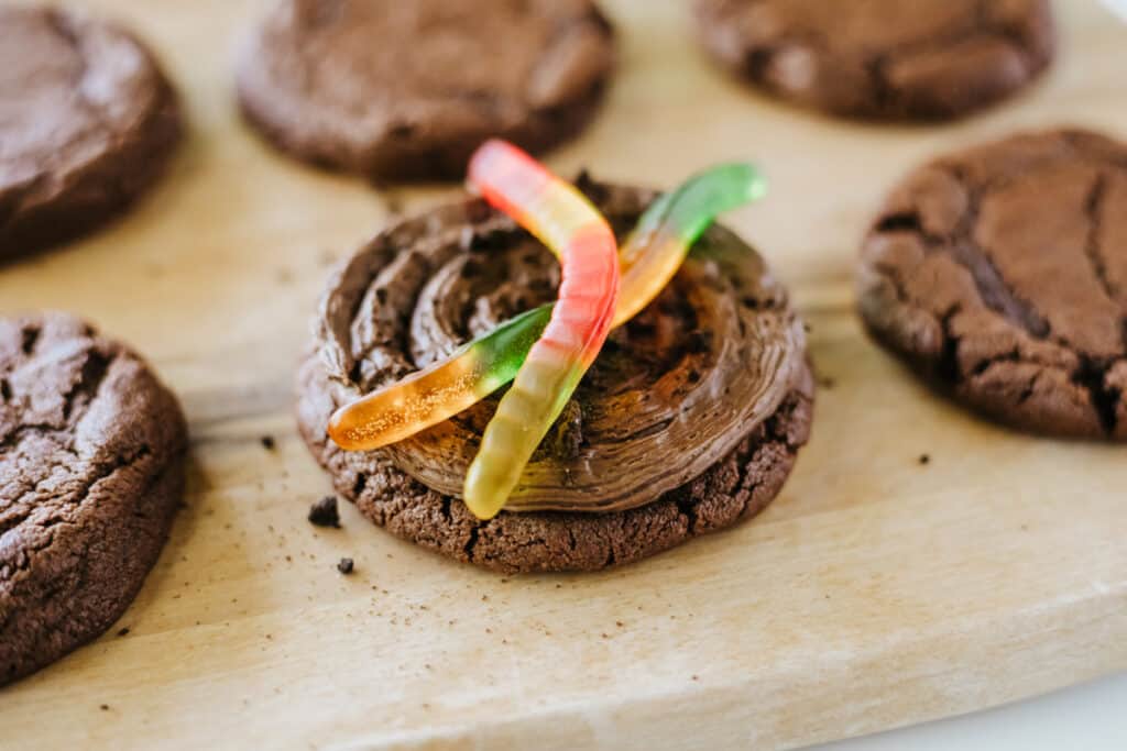 Close up of Copycat Crumbl Dirt Cake Cookies with chocolate icing, Oreo cookie crumbs, and gummy worms. 