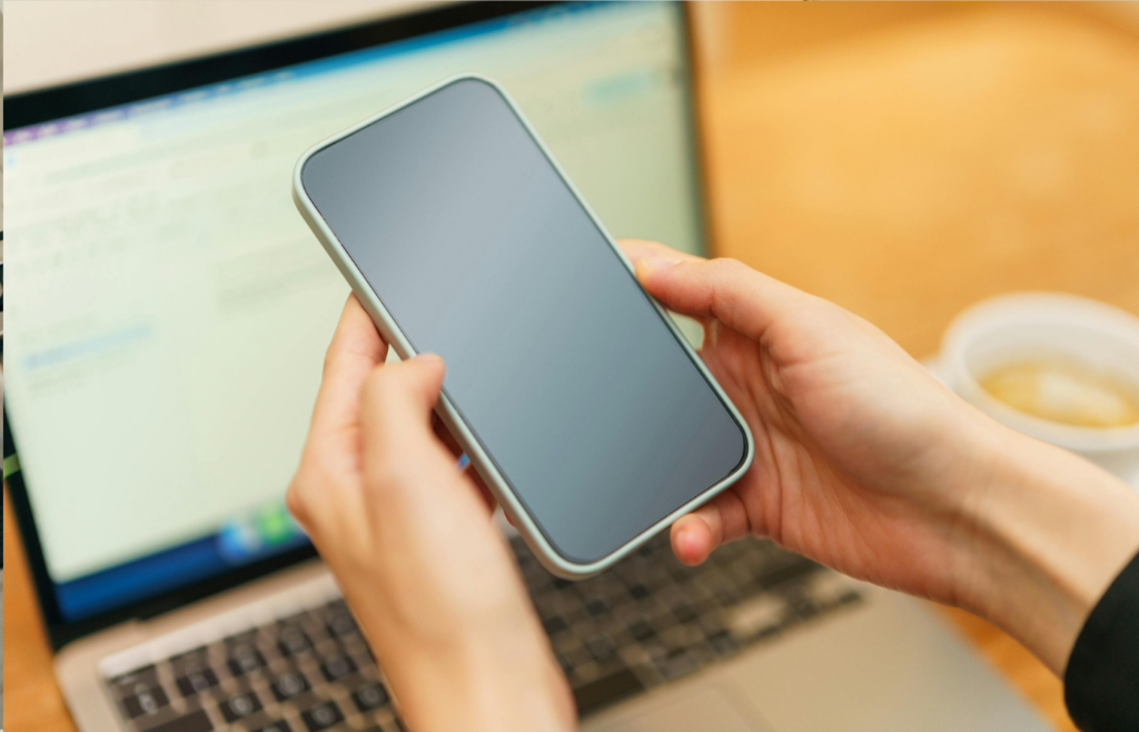 Hands Holding Smartphone Above Laptop screen showing 